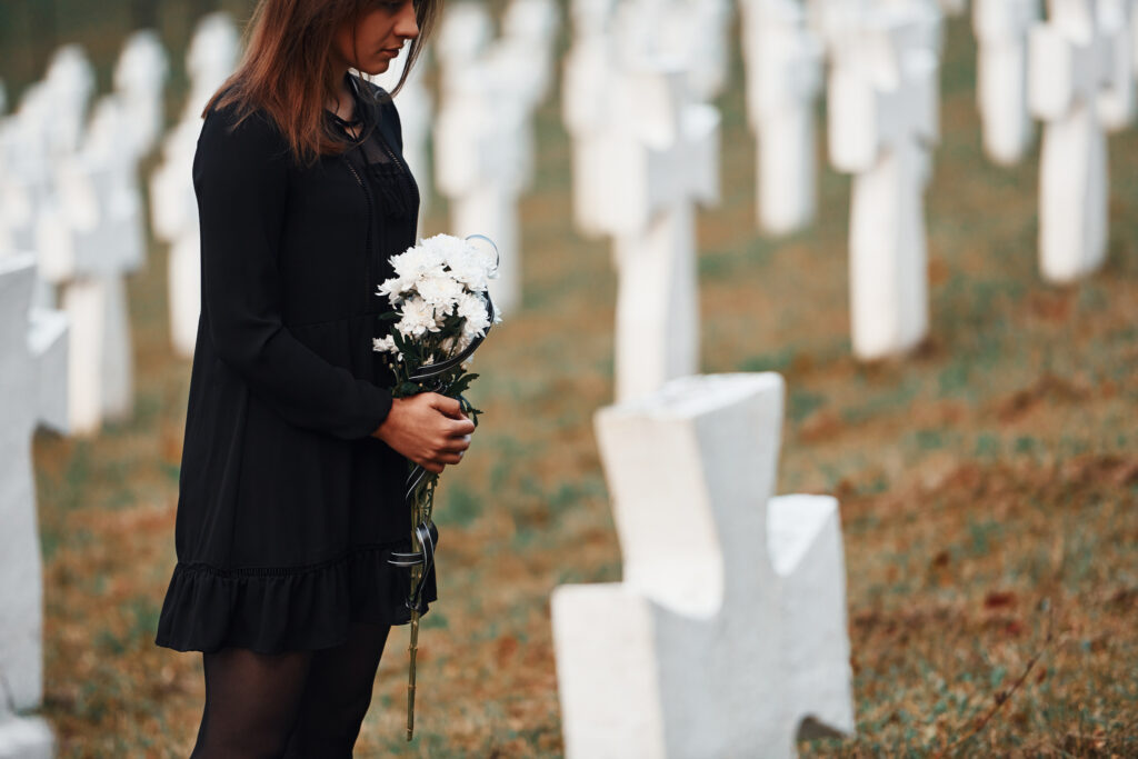 Young woman in black clothes visiting cemetery with many white crosses