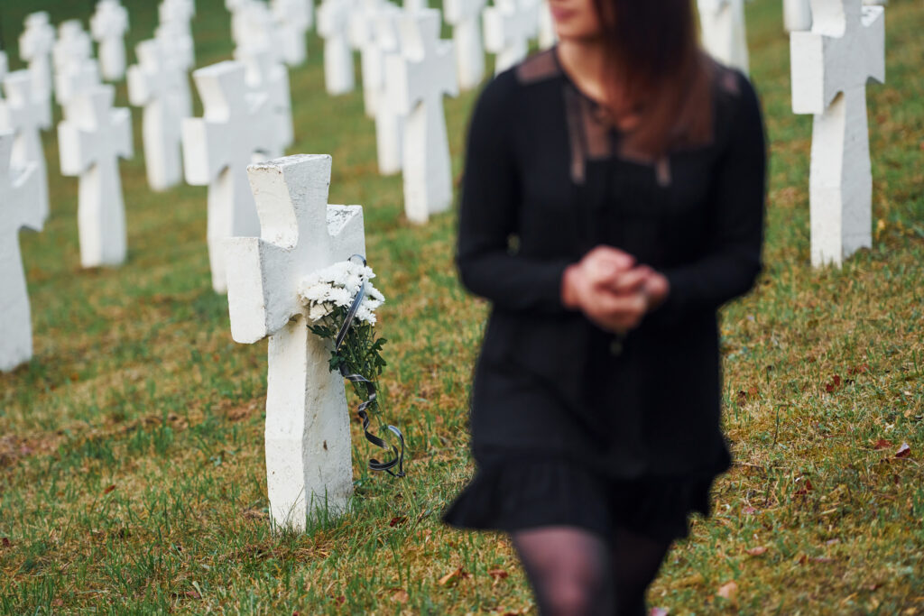 Young woman in black clothes visiting cemetery with many white crosses.