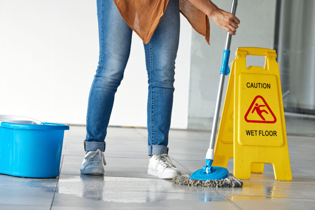 Cleaning, wet floor caution and woman mopping in building for maintenance